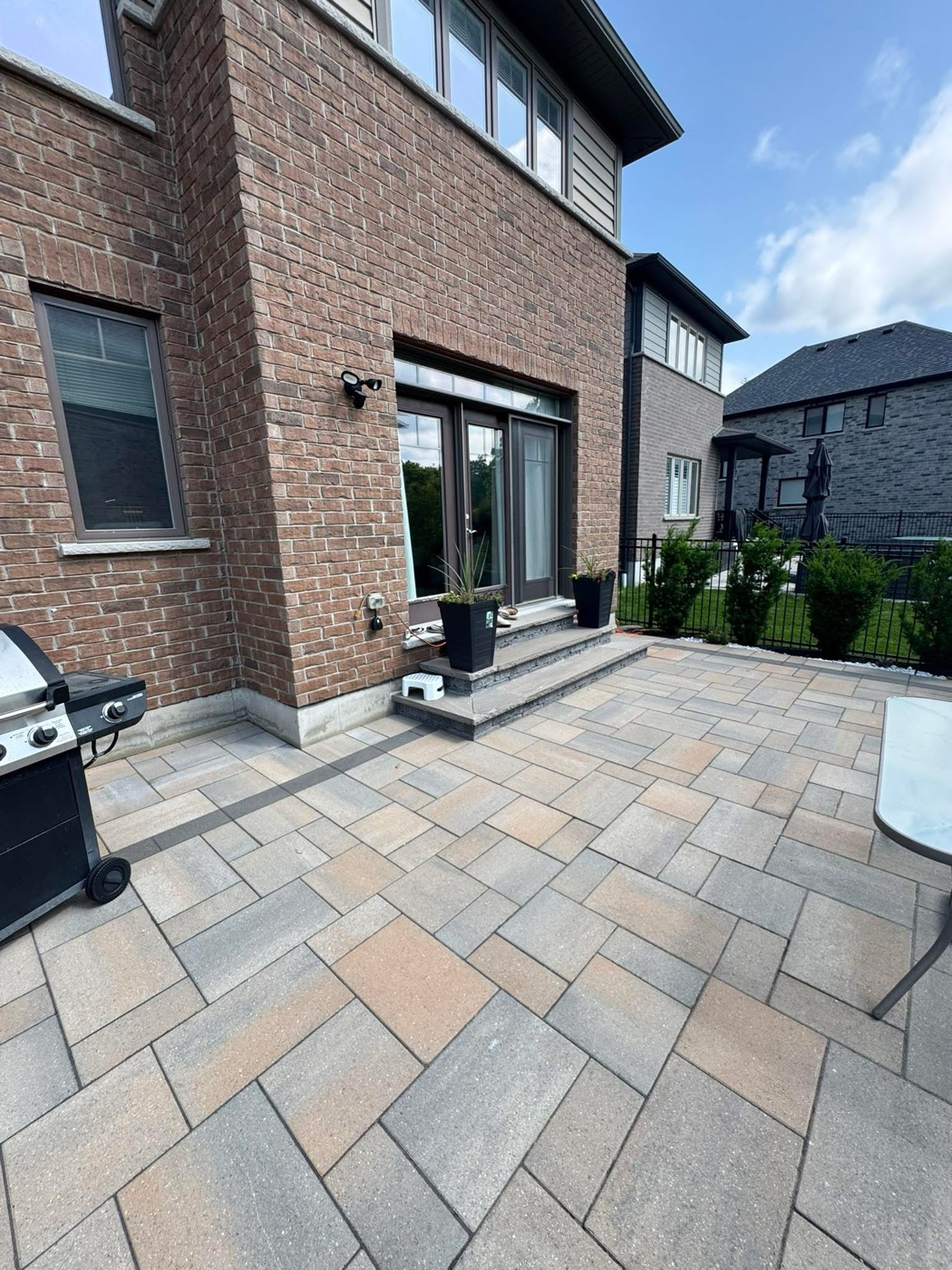 Paver patio with grill and seating alongside a brick home